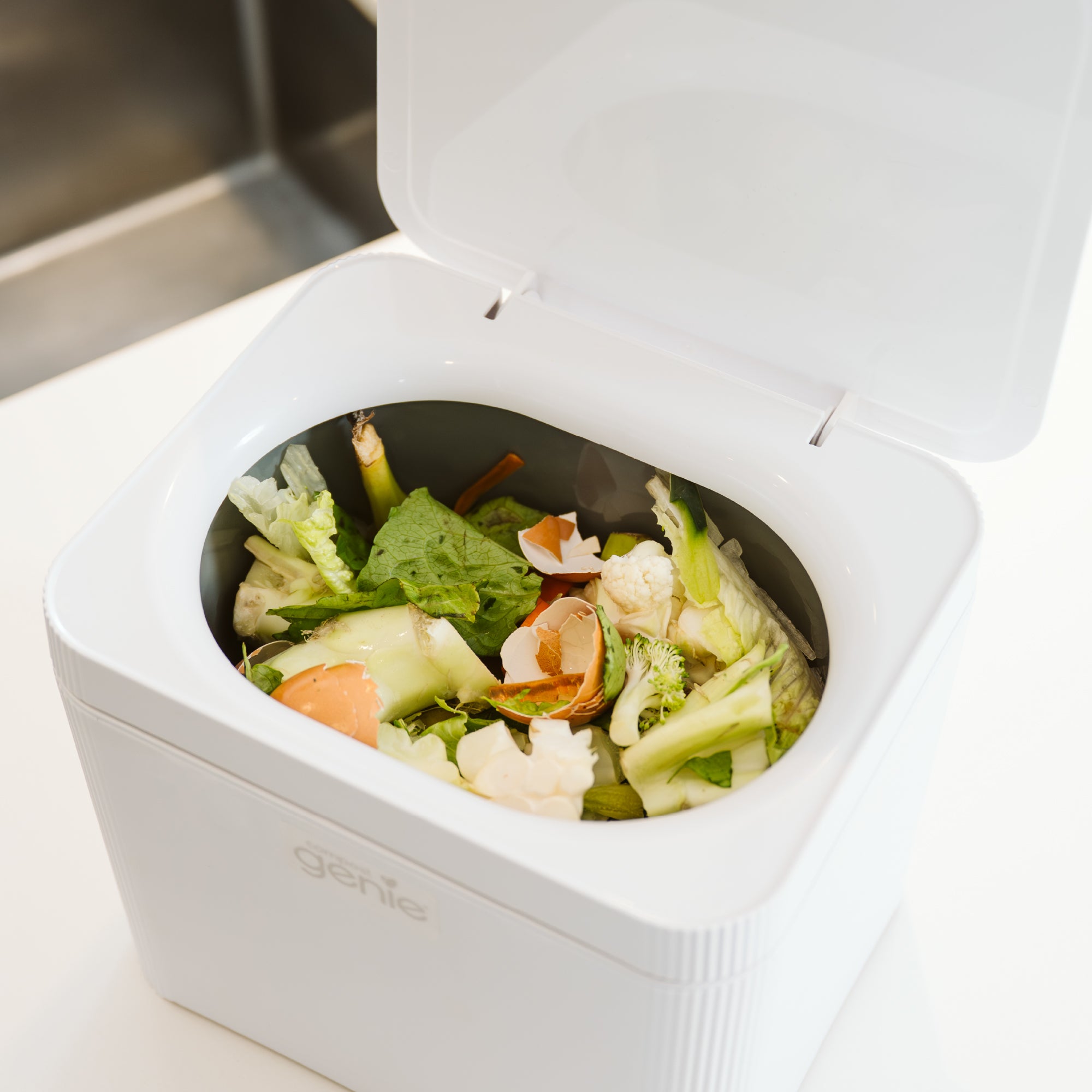 White compost bin filled with food waste on a kitchen counter_FR-FR
